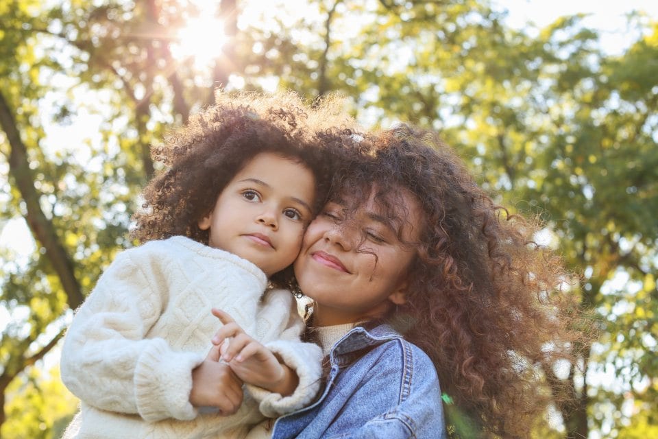 A mother and her daughter outdoors in warm afternoon light